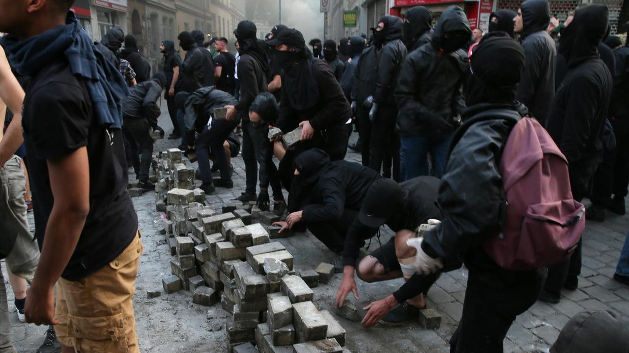Die schwarzgekleideten und teils vermummten Demonstranten errichten mehrere Stapel Pflastersteine, die sie aus dem Straßenbelag ziehen. Die schwarzgekleideten und teils vermummten Demonstranten errichten mehrere Stapel Pflastersteine, die sie aus dem Straßenbelag ziehen.