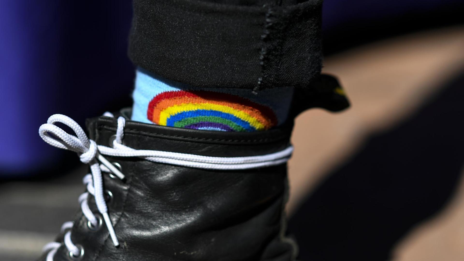 Detailaufnahme einer Regenbogen-Socke, die zwischen schwarzen Stiefeln und Hosen herausschaut. Detailaufnahme einer Regenbogen-Socke, die zwischen schwarzen Stiefeln und Hosen herausschaut.
