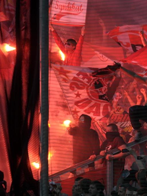 Fußballfans im Stadion zünden Bengalos und Feuerwerkskörper.