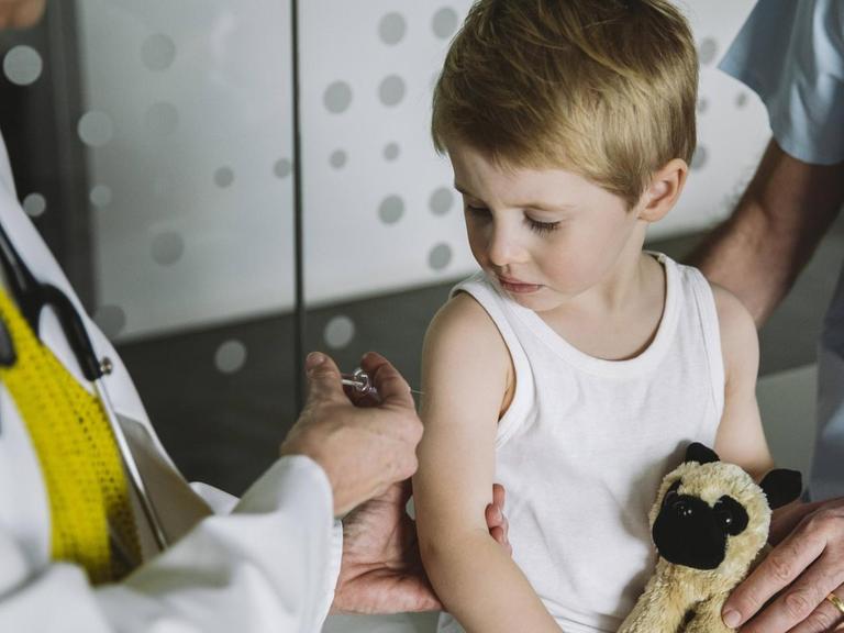 Eine Kinderärztin setzt einem Kleinkind in weißem Unterhemd eine Spritze in den Oberarm.