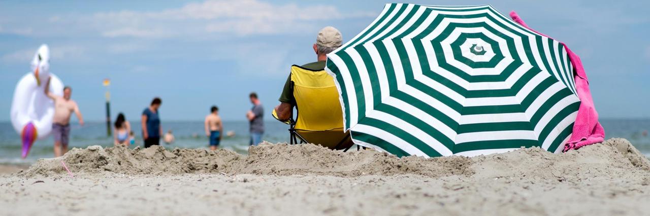 Urlauber sitzen bei hochsommerlichen Temperaturen unter einem Sonnenschirm am Strand von Norderney.