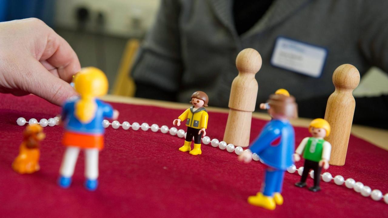 Verschiedene Playmobil und Holzfigürchen werden im Rahmen einer Therapiesitzung auf einer Oberfläche angeordnet. Verschiedene Playmobil und Holzfigürchen werden im Rahmen einer Therapiesitzung auf einer Oberfläche angeordnet.