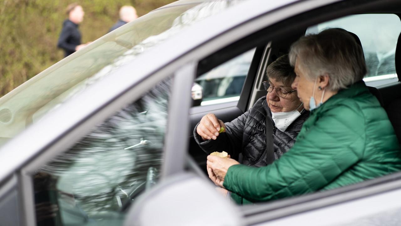 Zwei Besucherinnen teilen in ihren Auto während des KFZ-Gottesdienstes auf dem Kirmesplatz im Stadtteil Gnadental das Abendmahl. Die Kirchengemeinde Neuss-Süd veranstaltete Karfreitag einen Autokino-Gottesdienst unter Berücksichtigung der Corona-Schutzverordnung. Zwei Besucherinnen teilen in ihren Auto während des KFZ-Gottesdienstes auf dem Kirmesplatz im Stadtteil Gnadental das Abendmahl. Die Kirchengemeinde Neuss-Süd veranstaltete Karfreitag einen Autokino-Gottesdienst unter Berücksichtigung der Corona-Schutzverordnung.