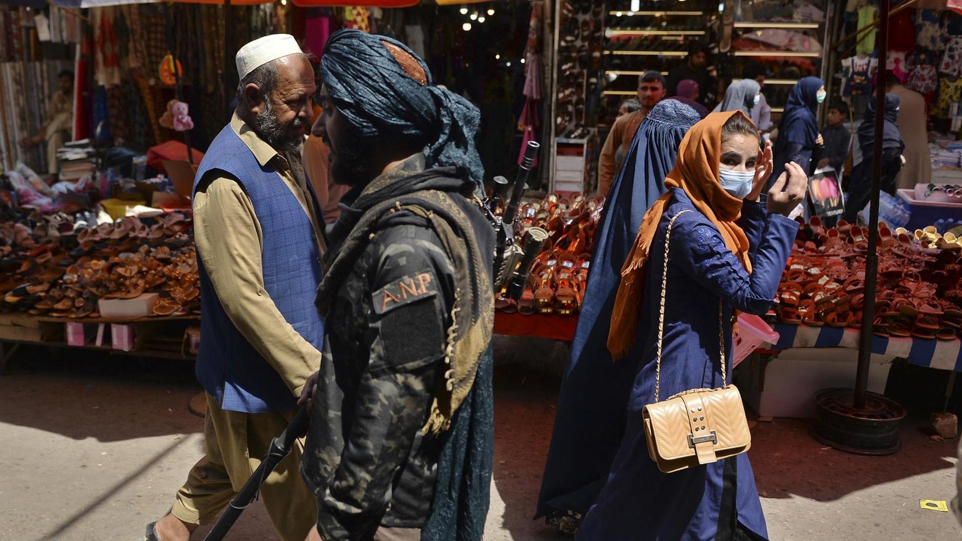 Taliban-Kämpfer gehen an Frauen mit Schleiern vorbei. Taliban-Kämpfer gehen an Frauen mit Schleiern vorbei.