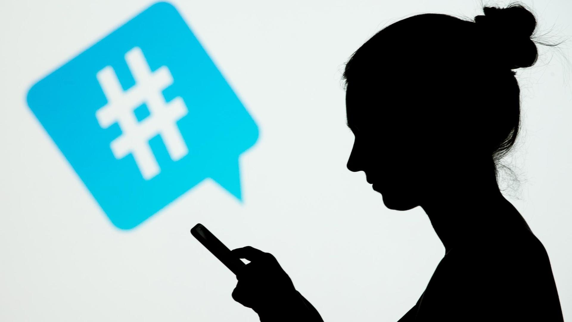 Die Silhouette einer Frau, die ein Smartphone in den Haenden haelt, ist am 08.01.2015 in Berlin vor dem Symbol eines Hashtags des sozialen Netzwerks Twitter zu sehen. Die Silhouette einer Frau, die ein Smartphone in den Haenden haelt, ist am 08.01.2015 in Berlin vor dem Symbol eines Hashtags des sozialen Netzwerks Twitter zu sehen.