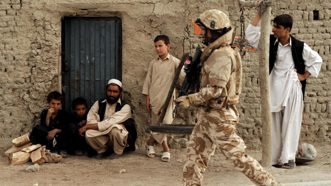 Ein Soldat der ISAF-Truppen in Afghanistan marschiert mit einem Maschiniengewehr durch Kabul während er von Männern am Straßenrand beobachtet wird Ein Soldat der ISAF-Truppen in Afghanistan marschiert mit einem Maschiniengewehr durch Kabul während er von Männern am Straßenrand beobachtet wird