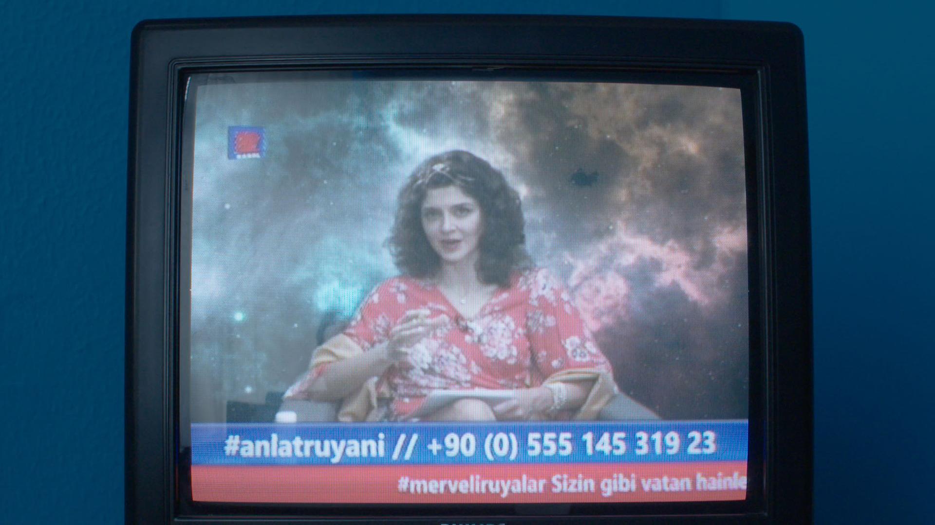 In einer Szene der fiktiven türkischen Seifenoper "Kanal 82" ist auf einem Fernsehbildschirm eine Frau zu sehen, die in die Kamera spricht, es ist eine Telefonnummer eingeblendet.