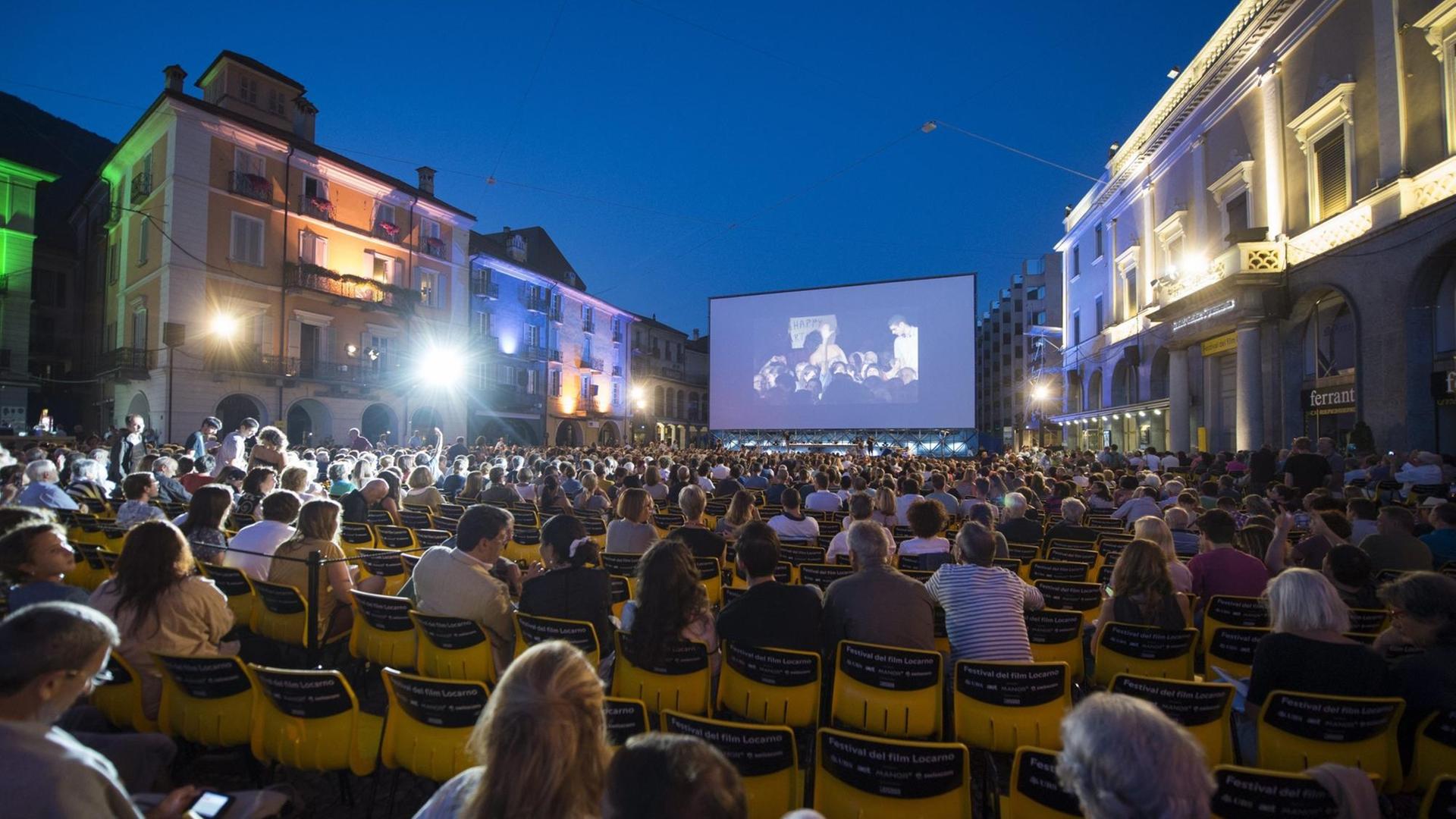 Zuschauer sitzen in der Nacht vor der offiziellen Eröffnung des Filmfestivals vor einer großen Leinwand mitten in Locarno Zuschauer sitzen in der Nacht vor der offiziellen Eröffnung des Filmfestivals vor einer großen Leinwand mitten in Locarno