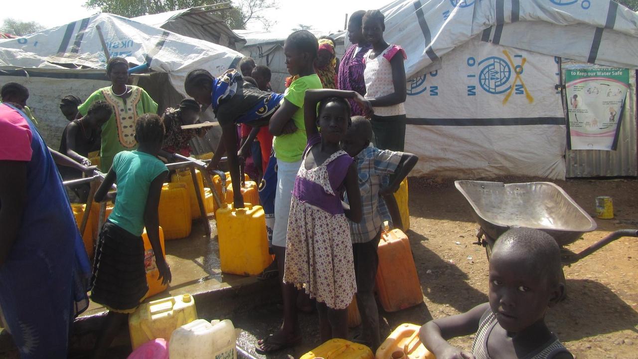 Frauen und Kinder stehen mit Eimern an mehreren Wasserhähnen im Flüchtlingslager. Frauen und Kinder stehen mit Eimern an mehreren Wasserhähnen im Flüchtlingslager.