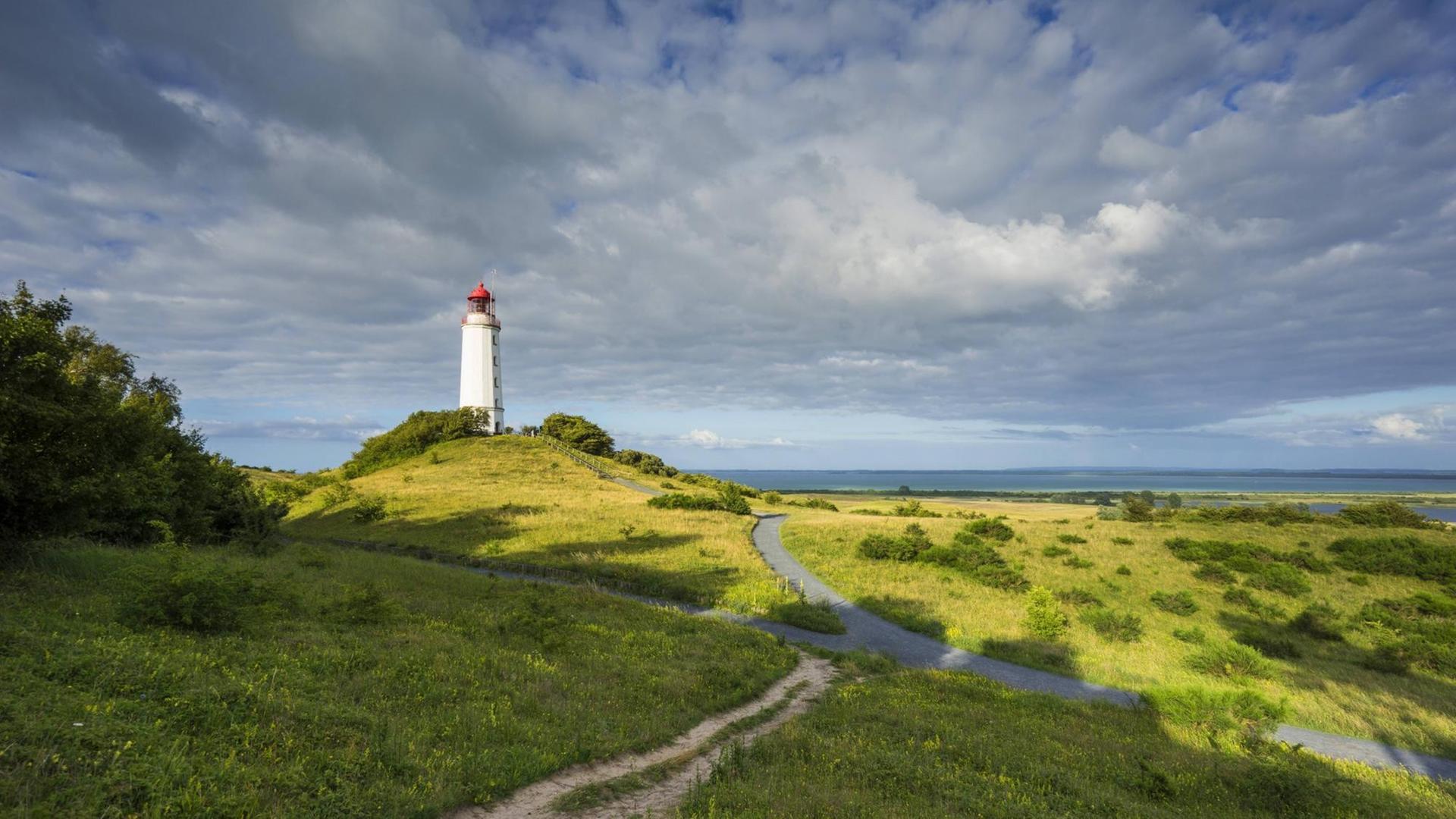 Der Leuchtturm von Hiddensee in einer grünen, hügeligen Landschaft mit Wolken am Himmel. Der Leuchtturm von Hiddensee in einer grünen, hügeligen Landschaft mit Wolken am Himmel.