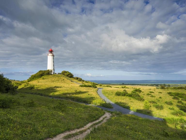 Der Leuchtturm von Hiddensee in einer grünen, hügeligen Landschaft mit Wolken am Himmel.