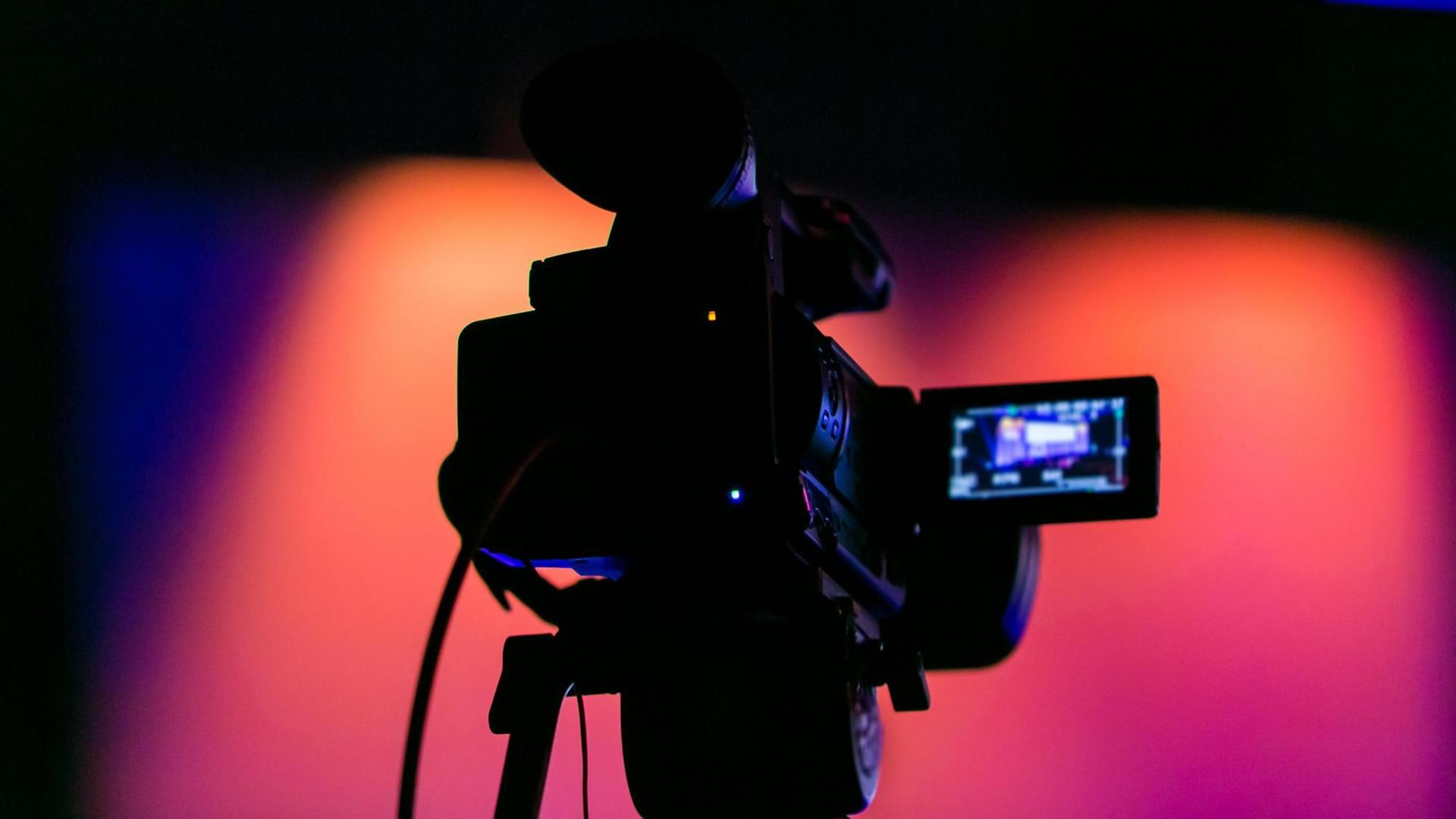 Silhouette einer Filmkamera vor bunten Bühnenlichtern Silhouette einer Filmkamera vor bunten Bühnenlichtern