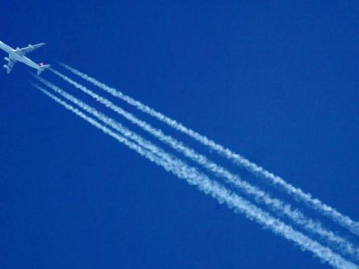 Ein Flugzeug hinterlässt Kondensstreifen vor einem blauen und wolkenlosen Himmel.