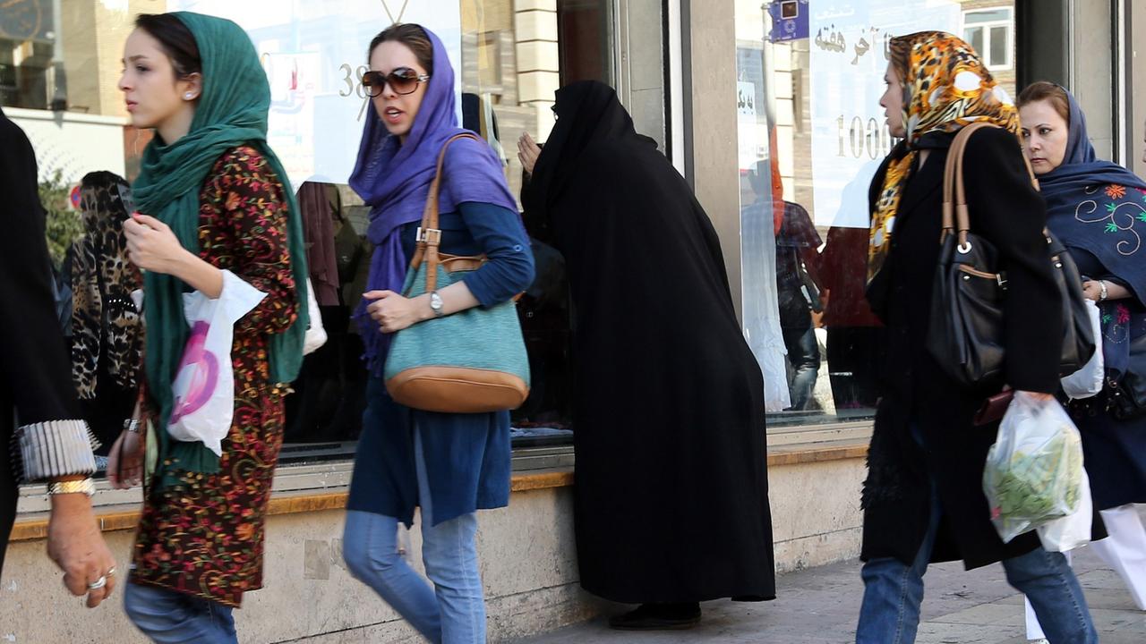 Junge Iranerinnen in Jeans und bunten Tüchern gehen mit Einkaufstüten eine Straße entlang. Junge Iranerinnen in Jeans und bunten Tüchern gehen mit Einkaufstüten eine Straße entlang.