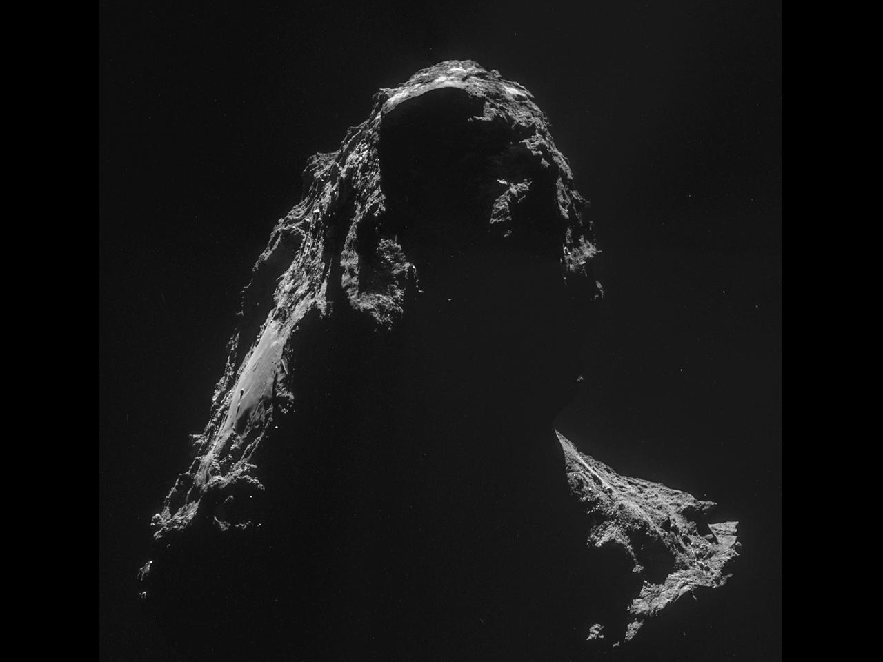 Eine Spitze des Kometenkerns ragt im grellen Licht der Sonne ins Bild. Die beleuchteten Flächen zeigen die zerklüftete Oberfläche, die schattigen Flächen liegen im nachtschwarzen Dunkel. 
