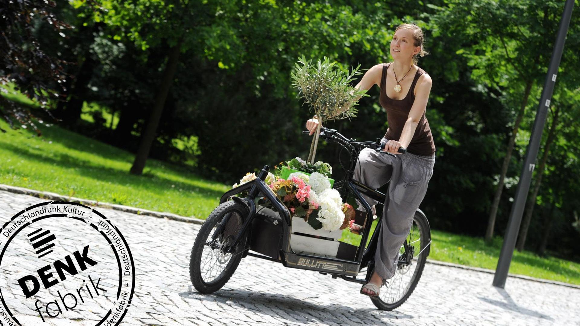 Eine Frau fährt mit einem Transportrad, das mit Blumen beladen ist. Mit Denkfabrik-Stempel Eine Frau fährt mit einem Transportrad, das mit Blumen beladen ist. Mit Denkfabrik-Stempel