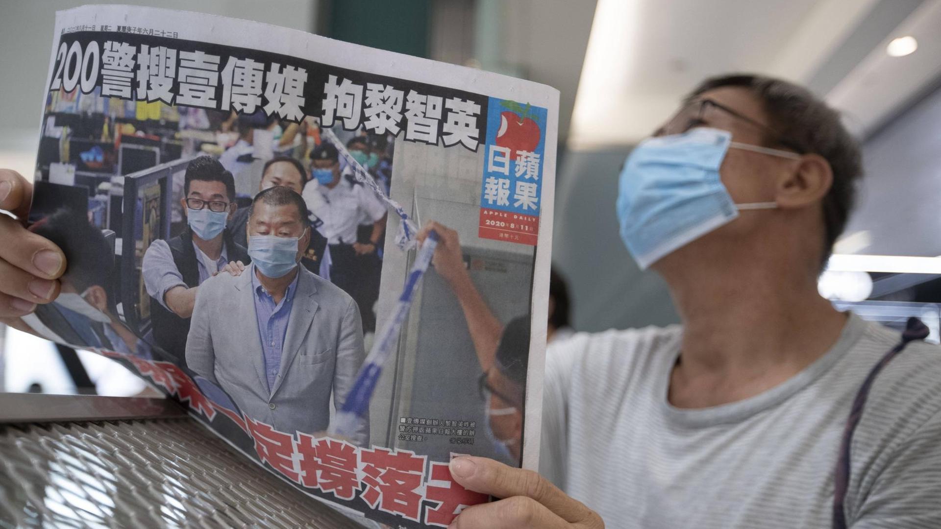 Ein Mann mit einem Mund-Nase-Schutz liest eine Ausgabe der "Apple Daily".