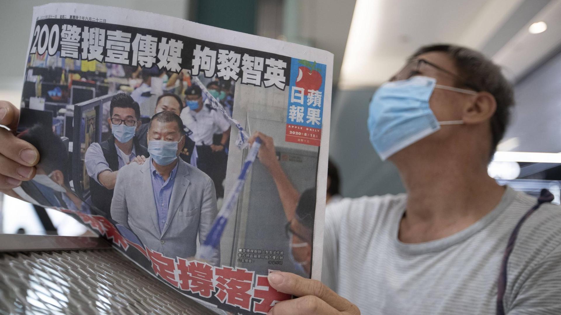 Ein Mann mit einem Mund-Nase-Schutz liest eine Ausgabe der "Apple Daily". Ein Mann mit einem Mund-Nase-Schutz liest eine Ausgabe der "Apple Daily".