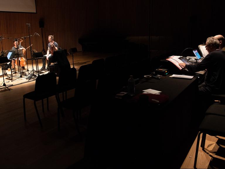 Links spielt das Quartett auf der Bühne und im Zuschauerraum sitzen Tonmeister an Bildschirmen, die den Sound live bearbeiten.