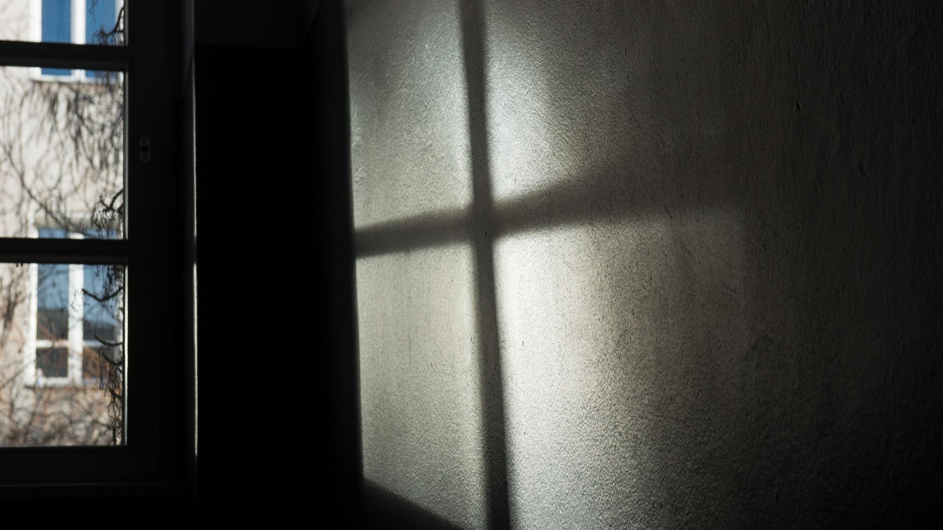 Ein Fenster wirft seinen Schatten auf die Wand. Es entsteht ein dunkles Kreuz. Ein Fenster wirft seinen Schatten auf die Wand. Es entsteht ein dunkles Kreuz.