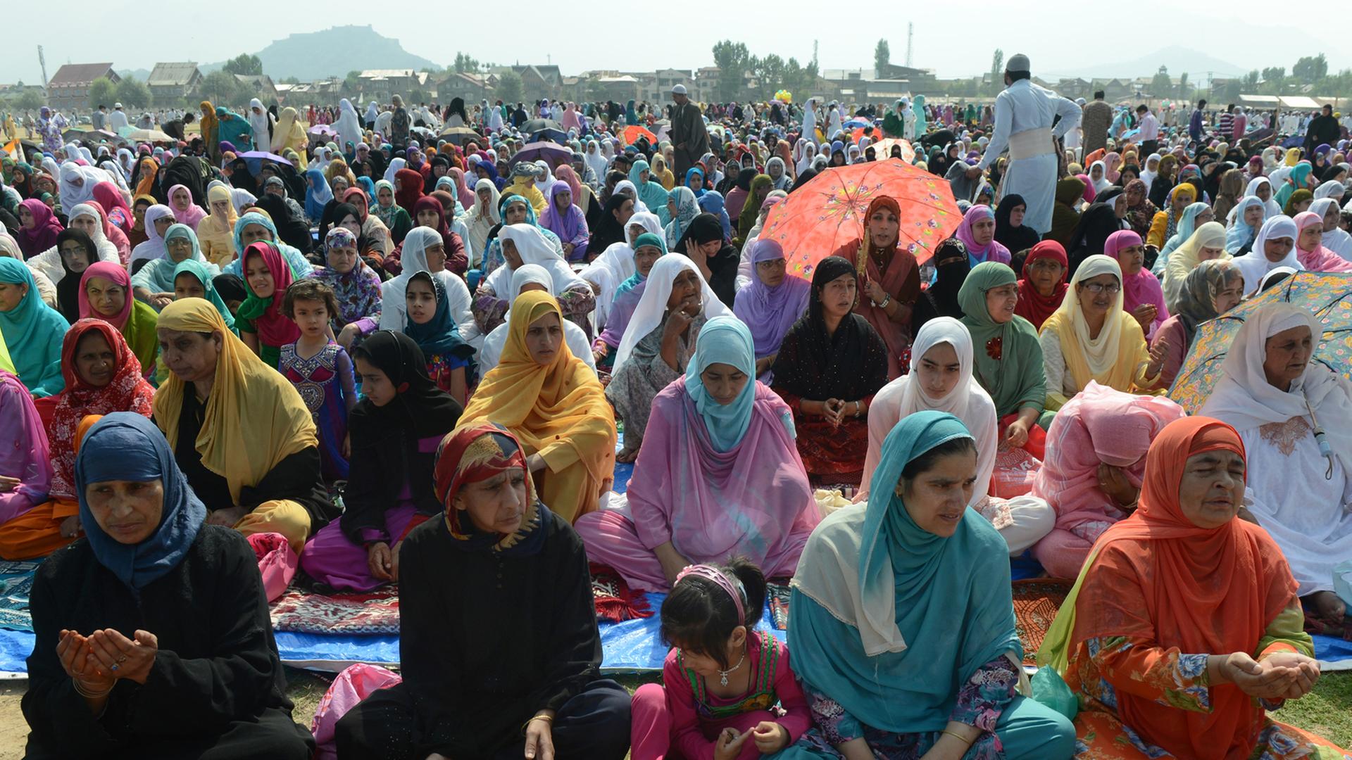 Indische Muslime sitzen auf dem Boden in Reihen hintereinander und beten, viele in bunten Gewändern.
