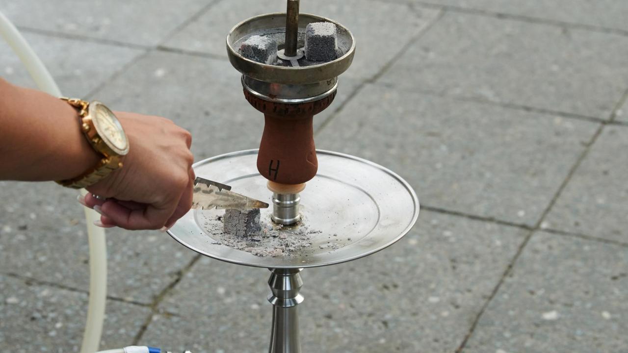 Ein Gast in einer Shisha Bar legt den abgebrannten Kohlewürfel auf den Teller. Ein Gast in einer Shisha Bar legt den abgebrannten Kohlewürfel auf den Teller.