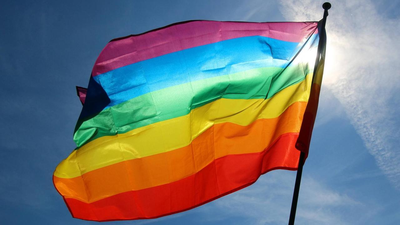 Regenbogenflagge mit Sonnenstrahlen im Gegenlicht Regenbogenflagge mit Sonnenstrahlen im Gegenlicht