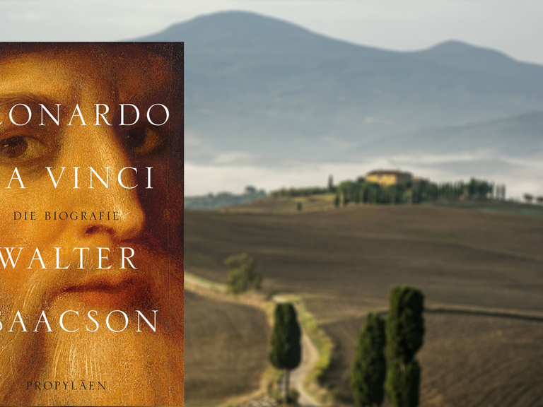 Im Vordergrund das Buchcover von Walter Isaacsons "Leonardo da Vinci", im Hintergrund unscharf eine Landschaft in der Toskana.