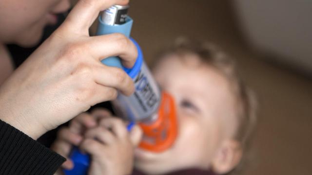 Eine Frau haelt ihrem Kind ein Asthmaspray vor den Mund (gestellte Szene), Kind ist unscharf