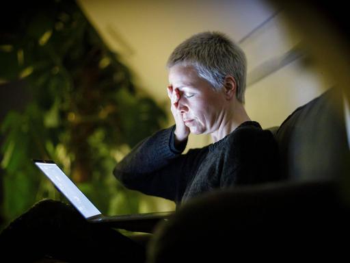 Eine Frau sitzt mit geschlossenen Augen auf dem Sofa vor ihrem Laptop und hat ihre Hand auf die Stirn gelegt. Symbolbild.