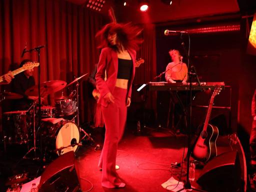 Sophie Auster tanzt auf der Bühne des Berliner "Privatclub", während ihre Musiker um sie herum spielen. Die Bühne wird von roten Scheinwerfern angestrahlt.