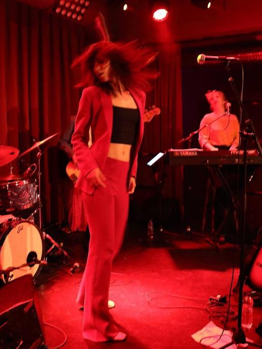 Sophie Auster tanzt auf der Bühne des Berliner "Privatclub", während ihre Musiker um sie herum spielen. Die Bühne wird von roten Scheinwerfern angestrahlt.