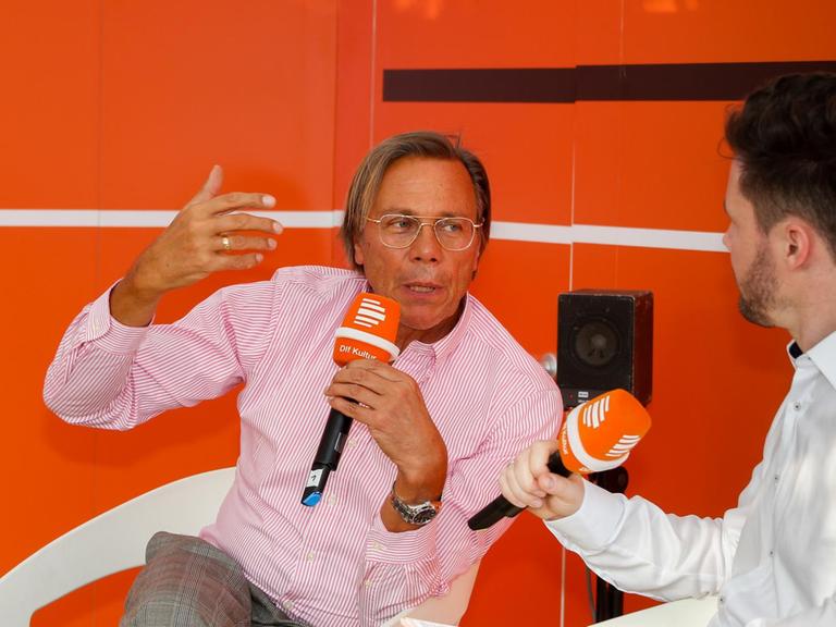 Harald Wetzler ist dem Moderator Christian Rabhansl zugewandt, er gestikuliert mit seiner Wand.