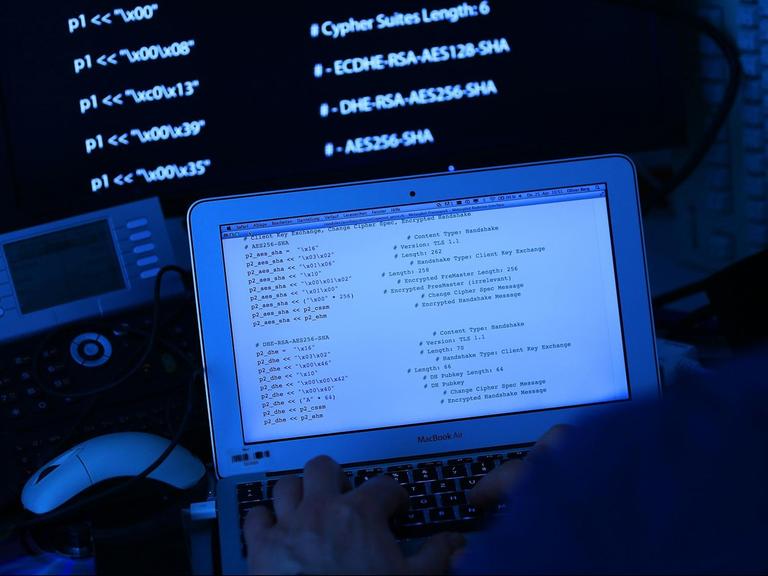 Ein Mann sitzt vor einem Rechner mit Computer Quellcode auf dem Bildschirm.