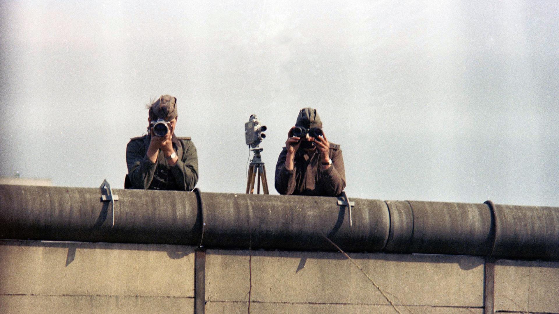 1976: Zwei Ostberliner Grenzposten fotografieren von der Mauer aus Menschen in Westberlin. 1976: Zwei Ostberliner Grenzposten fotografieren von der Mauer aus Menschen in Westberlin.