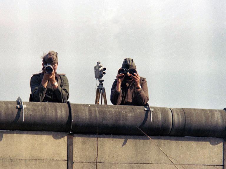 1976: Zwei Ostberliner Grenzposten fotografieren von der Mauer aus Menschen in Westberlin.