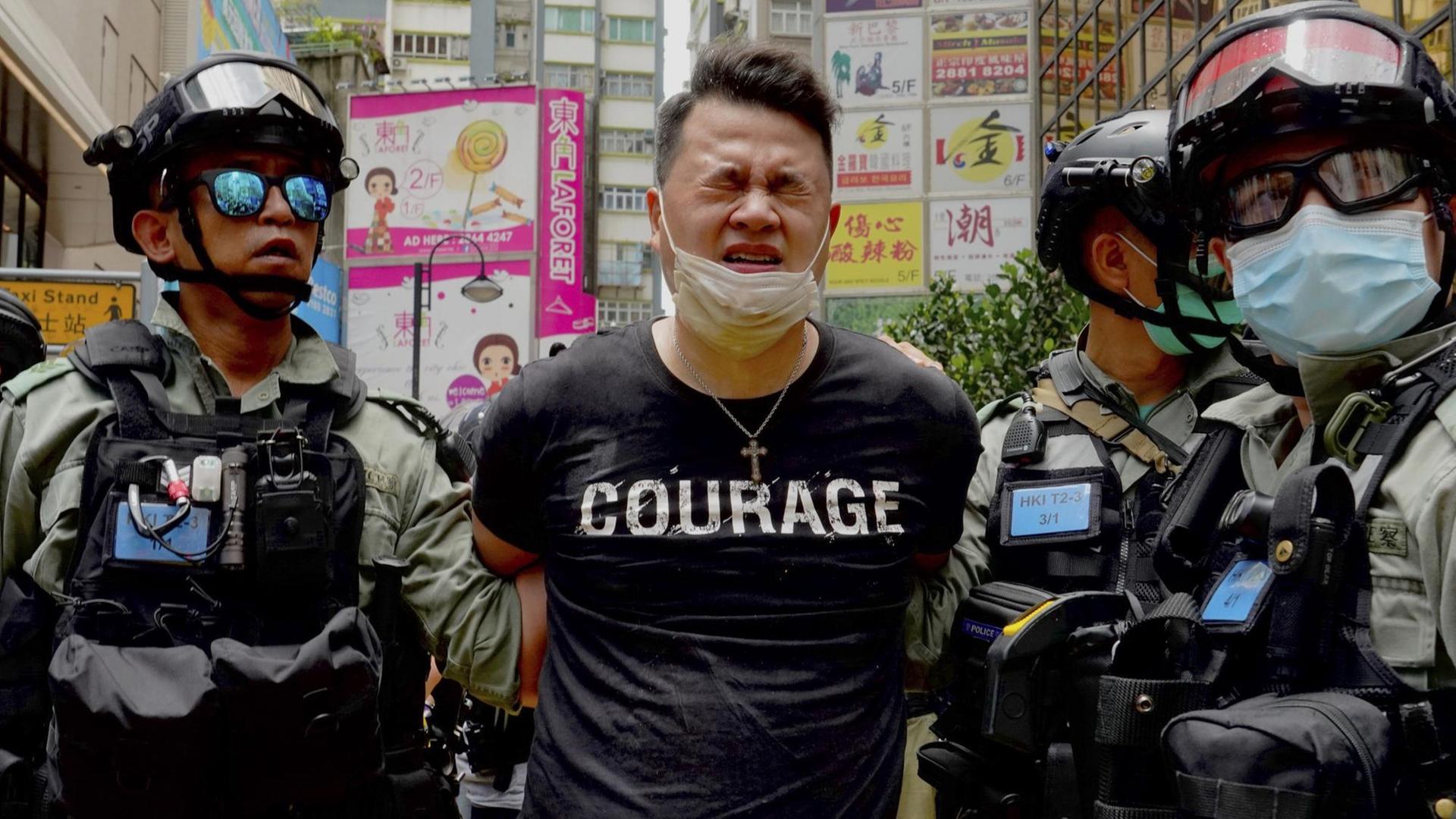 Ein Demonstrant wird in Hongkong von zwei Polizisten abgeführt. Auf dem T-Shirt des Verhafteten ist "Courage" zu lesen. Ein Demonstrant wird in Hongkong von zwei Polizisten abgeführt. Auf dem T-Shirt des Verhafteten ist "Courage" zu lesen.