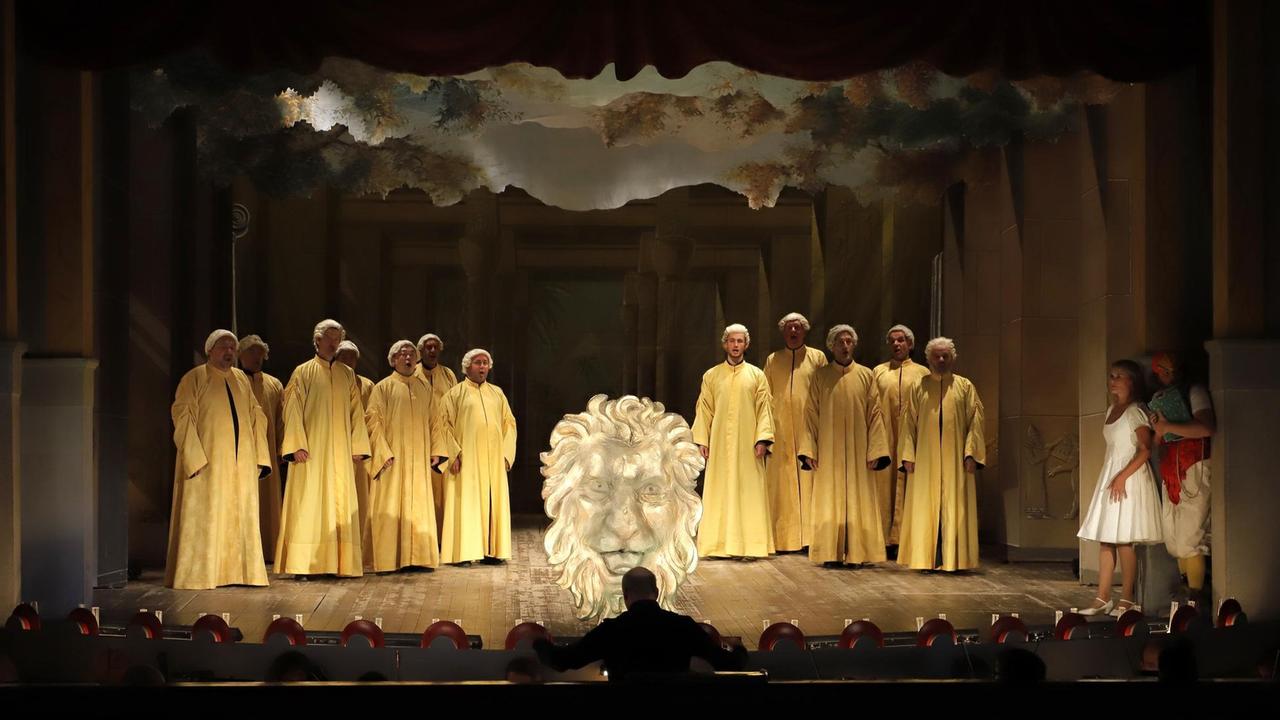 Ein Chor in gelben Gewändern steht an der historischen Bühnenrampe des Theaters.