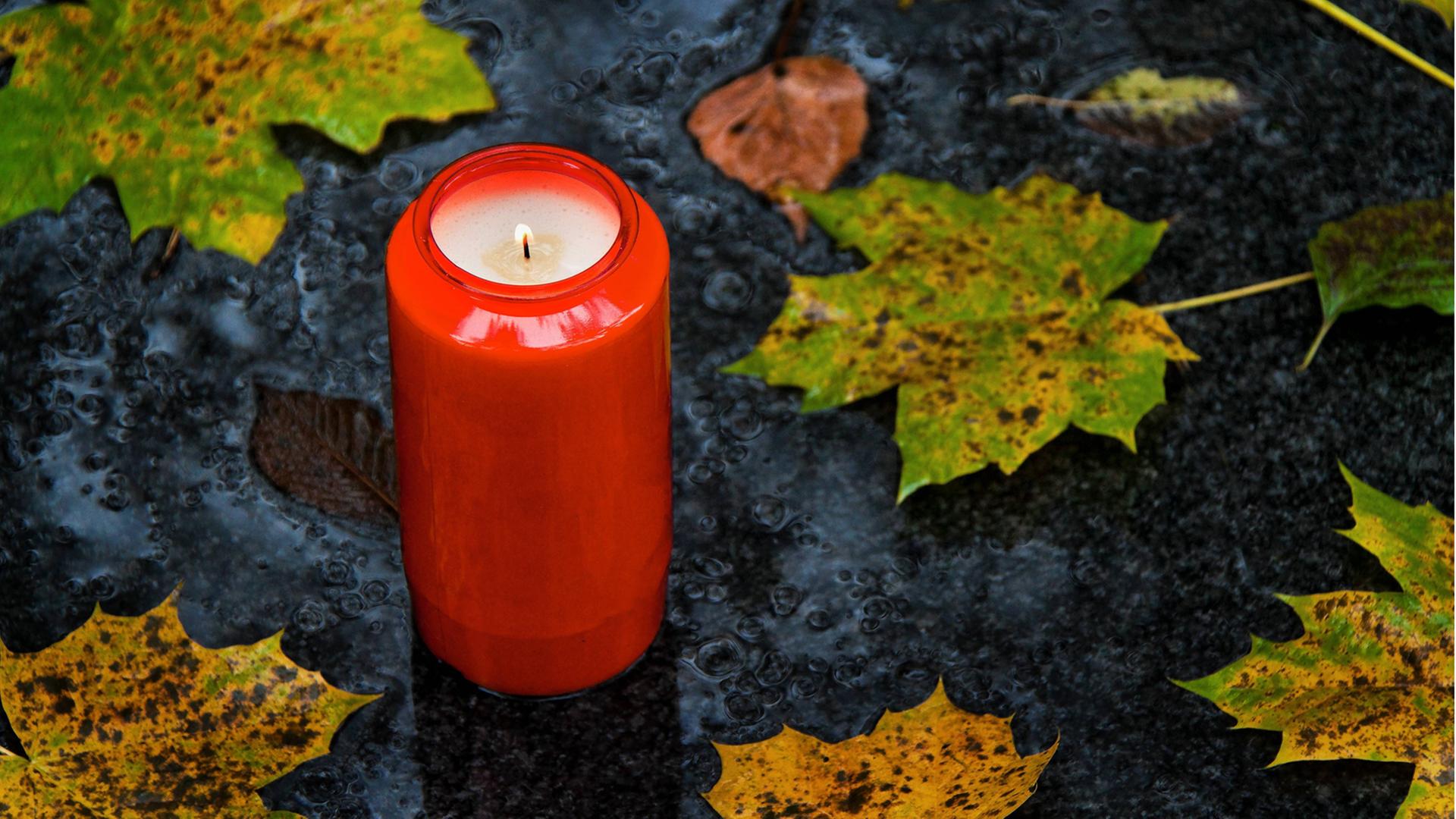 Ein Grablicht zu Allerheiligen im Herbst mit Blättern Ein Grablicht zu Allerheiligen im Herbst mit Blättern