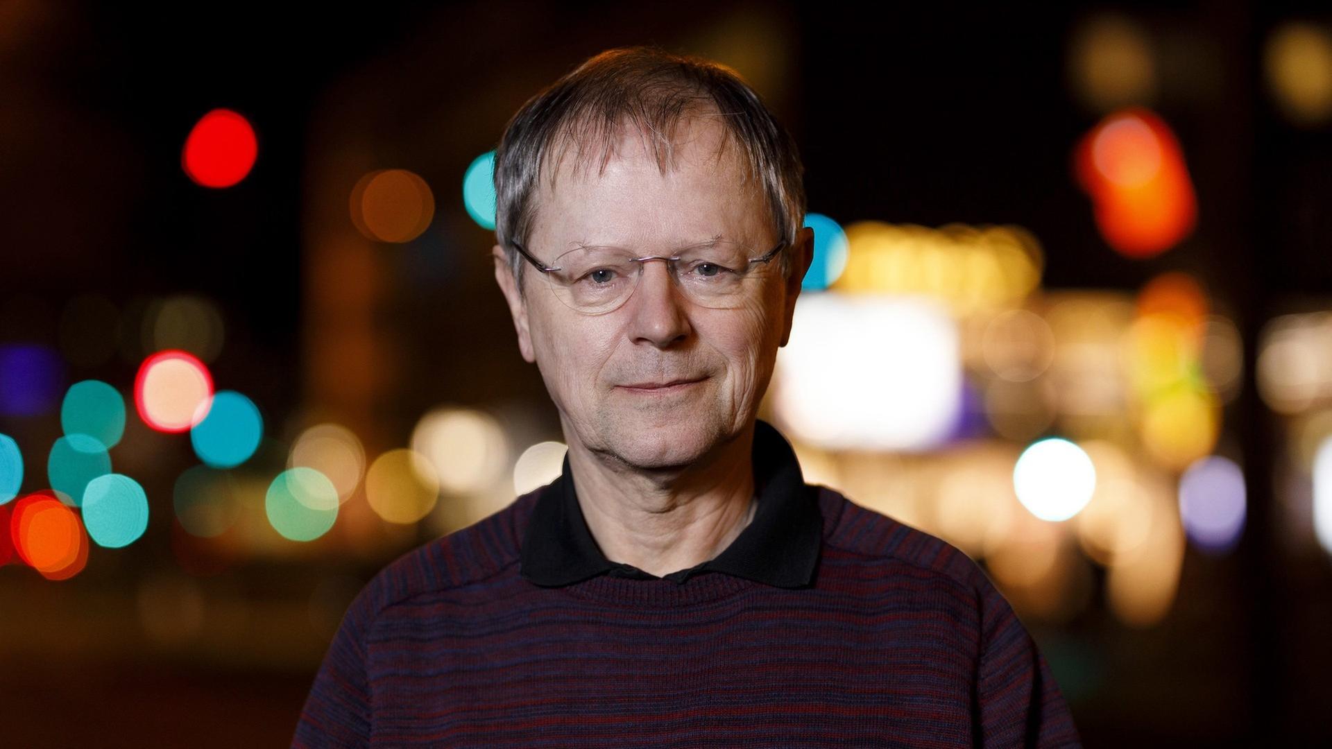 Ein Mann mit Brille, im Hintergrund sieht man verschwomme Stadtlichter in der Dunkelheit. Ein Mann mit Brille, im Hintergrund sieht man verschwomme Stadtlichter in der Dunkelheit.