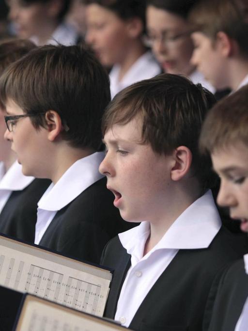 Eine Ausschnitt von singenden Jungen eines Knabenchors, alle sind festlich gekleidet und halten Noten in ihrern Händen.