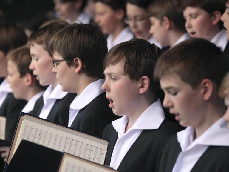 Eine Ausschnitt von singenden Jungen eines Knabenchors, alle sind festlich gekleidet und halten Noten in ihrern Händen.