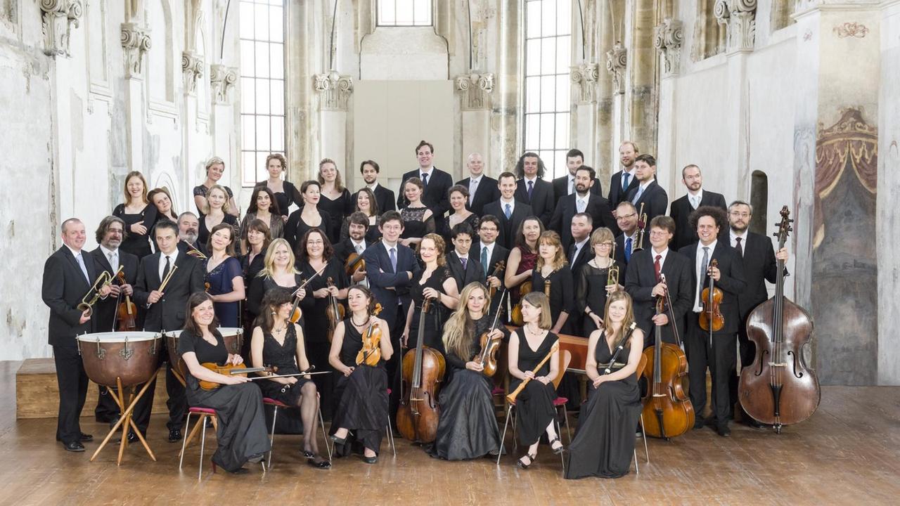 Ein Chor und ein Barockorchester stehen beieinander in einem großen, hellen Kirchenraum, der noch einige Wandbemalungen aufweist. Ein Chor und ein Barockorchester stehen beieinander in einem großen, hellen Kirchenraum, der noch einige Wandbemalungen aufweist.