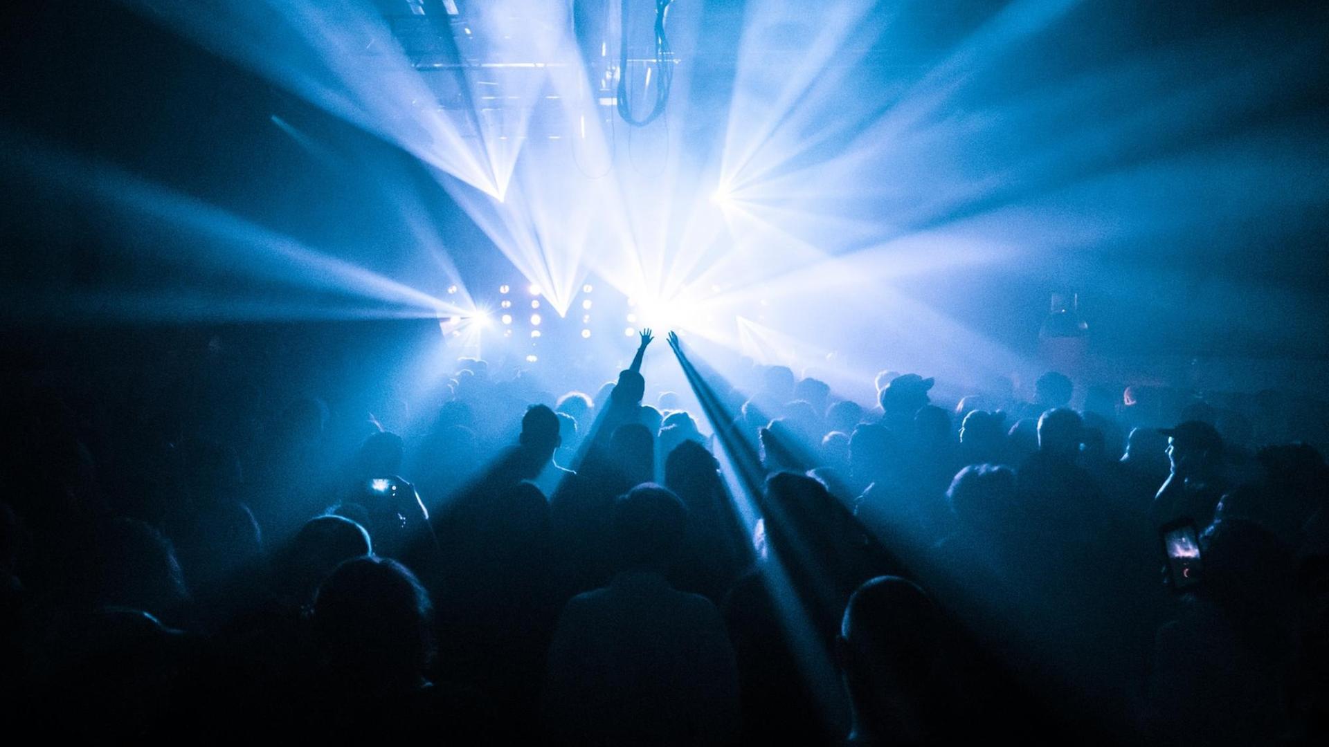 Menschen, die im Club tanzen und ihre Hände in die Höhe werfen; die Szene ist in blaues Laserlicht getaucht. Menschen, die im Club tanzen und ihre Hände in die Höhe werfen; die Szene ist in blaues Laserlicht getaucht.
