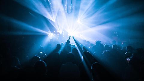 Menschen, die im Club tanzen und ihre Hände in die Höhe werfen; die Szene ist in blaues Laserlicht getaucht.