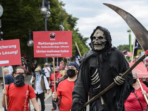 Rot gekleidete Protestierende der Veranstaltungsbranche ziehen durch Berlin, im Vordergrund ein als Sensenmann verkleideter Demonstrant