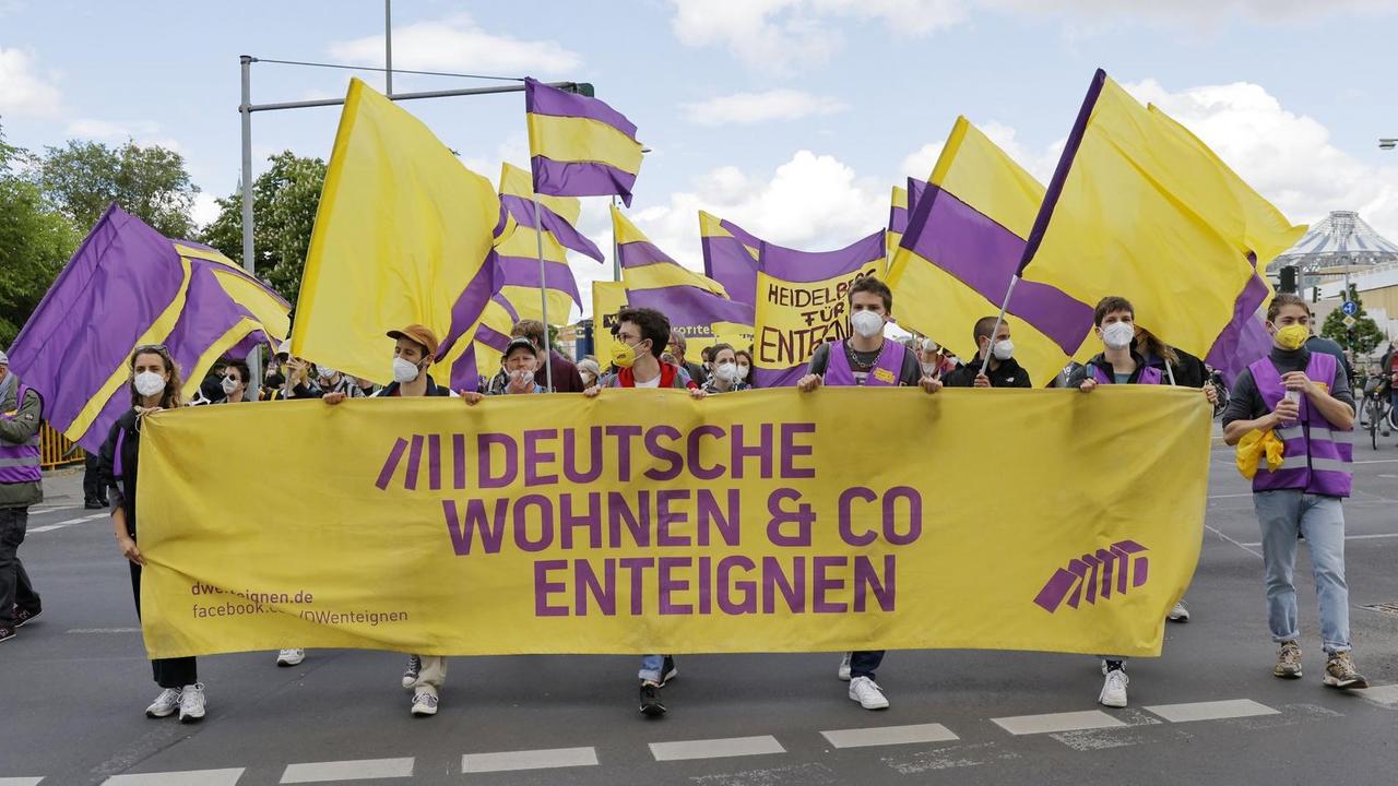 Demonstranten ziehen mit Fahnen und Bannern auf einer Straße entlang und fordern die Enteignung großer Wohnungskonzerne. Demonstranten ziehen mit Fahnen und Bannern auf einer Straße entlang und fordern die Enteignung großer Wohnungskonzerne.