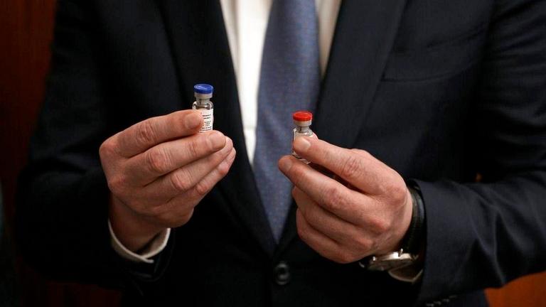 Nahaufmen eines Mannes im Anzug, der in seinen händen ein kleines Fläschchens hält, die Kappe des rechten ist blau, die des linken rot. Nahaufmen eines Mannes im Anzug, der in seinen händen ein kleines Fläschchens hält, die Kappe des rechten ist blau, die des linken rot.