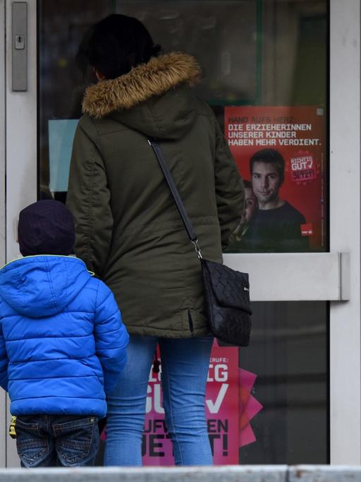 Eine Mutter steht mit ihrem Kind in Kassel (Hessen) vor einer geschlossenen Kita, an der Streik-Hinweise hängen
