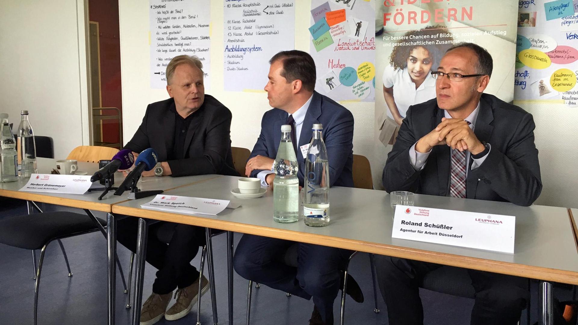 Drei Männer mittleren Alters sitzen an einem Tisch mit Mikrofonen vor sich. Sie werden gleich eine Pressekonferenz geben. Drei Männer mittleren Alters sitzen an einem Tisch mit Mikrofonen vor sich. Sie werden gleich eine Pressekonferenz geben.